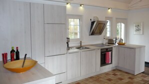 A modern kitchen with white cabinetry, a large island with a bowl, a stove, and a sink. - Landhaus Balu - fantastic half-timbered holiday home in Oberberg (Nümbrecht)