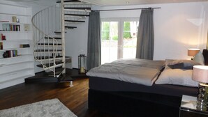A bedroom with a spiral staircase, a large bed, a bedside table with a lamp, and a bookshelf. - Landhaus Balu - fantastic half-timbered holiday home in Oberberg (Nümbrecht)