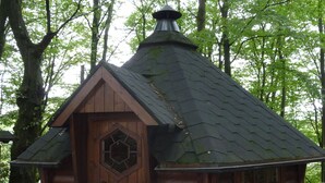 A small wooden cabin with a hexagonal window and a chimney, surrounded by trees. - Landhaus Balu - fantastic half-timbered holiday home in Oberberg (Nümbrecht)