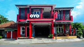 Un edificio de dos pisos con un llamativo letrero 'OYO', un acceso cubierto y un pequeño espacio al aire libre con plantas.