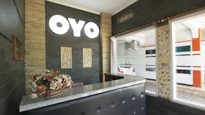 Una mesa de recepción con un gran letrero "OYO", un jarrón de flores y vistas a un tren a través de una puerta de cristal.