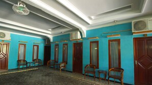 Una habitación con paredes azules, puertas de madera y suelo de baldosas. Hay varias sillas de madera y una pequeña mesa.