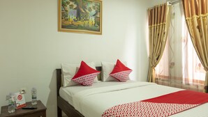 Habitación de hotel con cama, almohadas, un cuadro en la pared y cortinas.