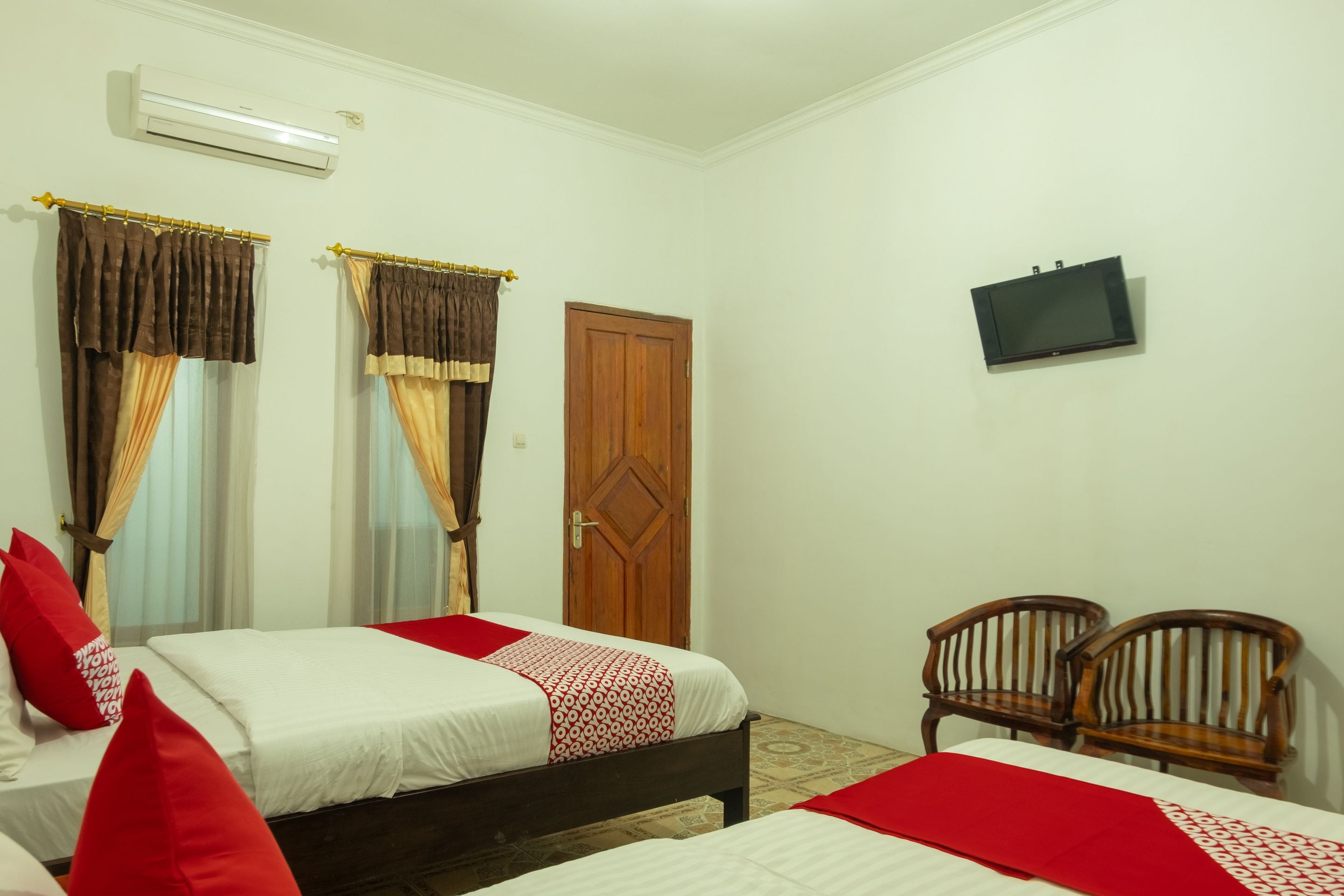A hotel room with two beds, a TV mounted on the wall, and a wooden door.