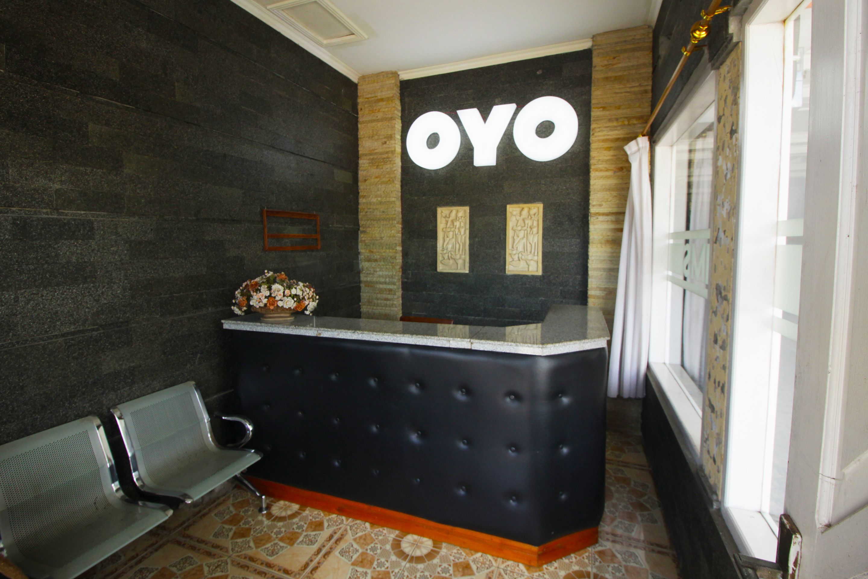 A reception desk with a 'OYO' sign, a bench, and a patterned floor.