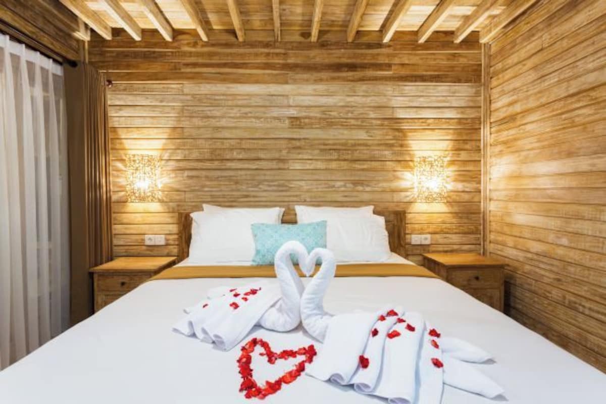 A wooden-paneled room with a bed, two bedside tables, and wall-mounted lights.