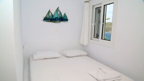 Ein Zimmer mit einem Einzelbett, weißer Bettwäsche, einem Fenster mit Meerblick und einer Wanddekoration mit Segelbooten.