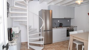 Eine kompakte Küche mit Edelstahlkühlschrank, Einbauofen und Spüle. Eine weiße Wendeltreppe führt zu einer weiteren Ebene.