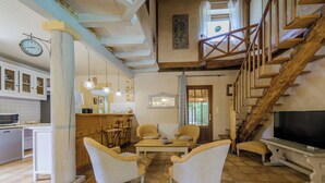 A spacious living area with a high ceiling, wooden staircase, and a kitchen with modern appliances.