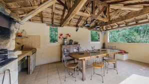 A rustic kitchen with a wooden table and chairs, a stone countertop, and a window with greenery outside.