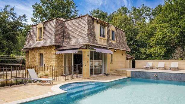 A stone house with a swimming pool, a covered patio, and a fenced garden area.