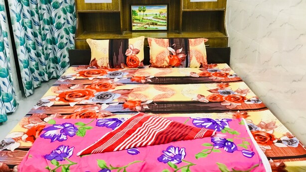Une chambre à coucher avec un lit, une literie à motifs floraux, une étagère avec des objets décoratifs et des rideaux.