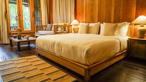 A spacious bedroom with a large bed, wooden walls, and a view of greenery through the windows. - Songtsam Linka Lijiang (Lijiang)