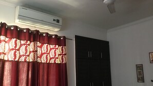 A room with a red curtain, a black wardrobe, and an air conditioning unit on the wall. - HomeNow - Full Kadambari - Botanical Garden Metro (Noida-)
