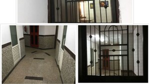 A corridor with a metal gate and a red door, leading to a room with a bed and a nightstand. - HomeNow - Full Kadambari - Botanical Garden Metro (Noida-)