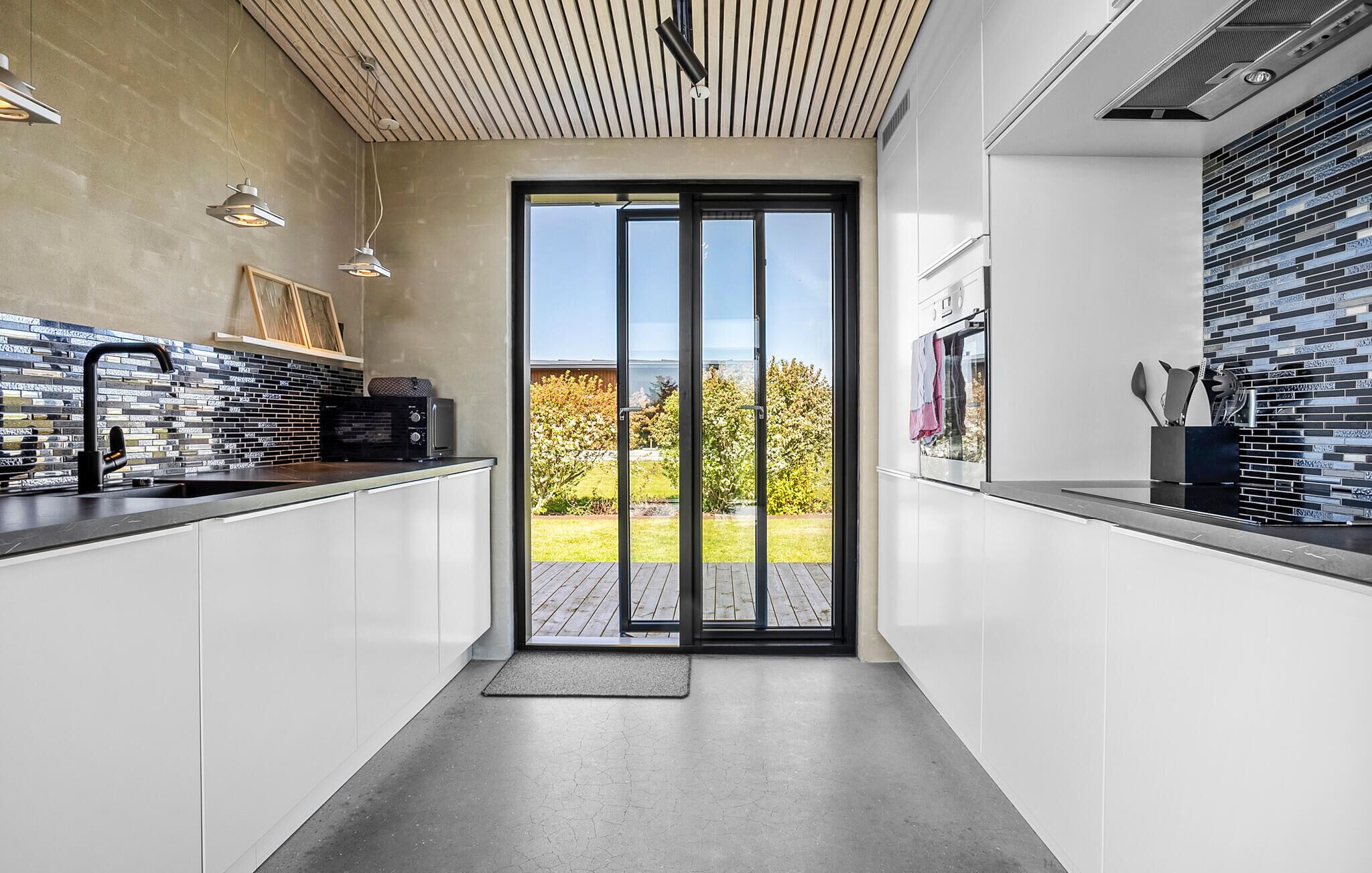 Een moderne keuken met een grote schuifpui naar een balkon, witte kasten en een zwart aanrecht.