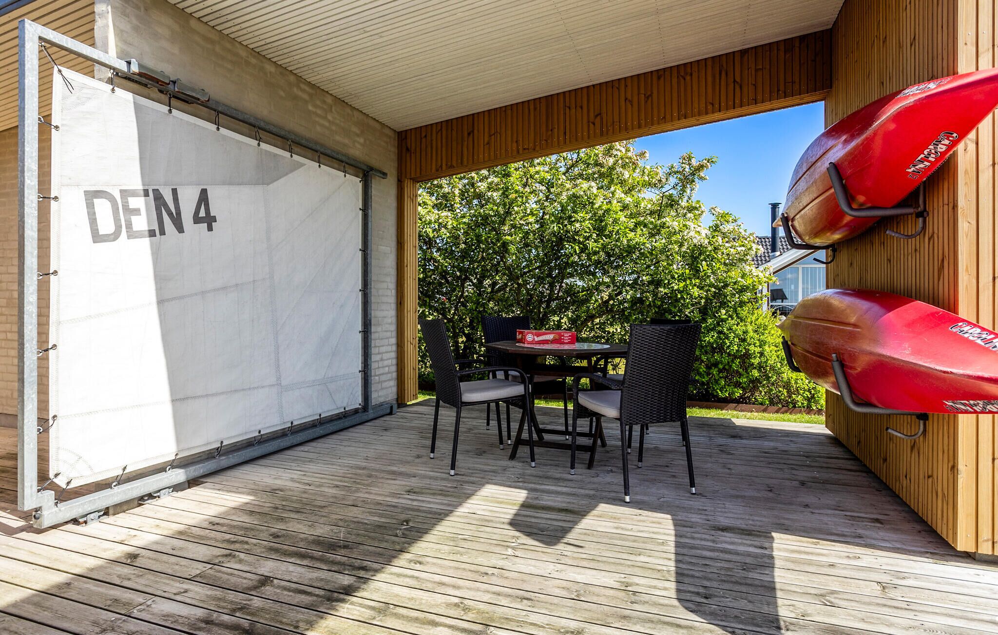 An outdoor patio with a table and chairs, a covered area with a 'DEN 4' sign, and a red kayak.