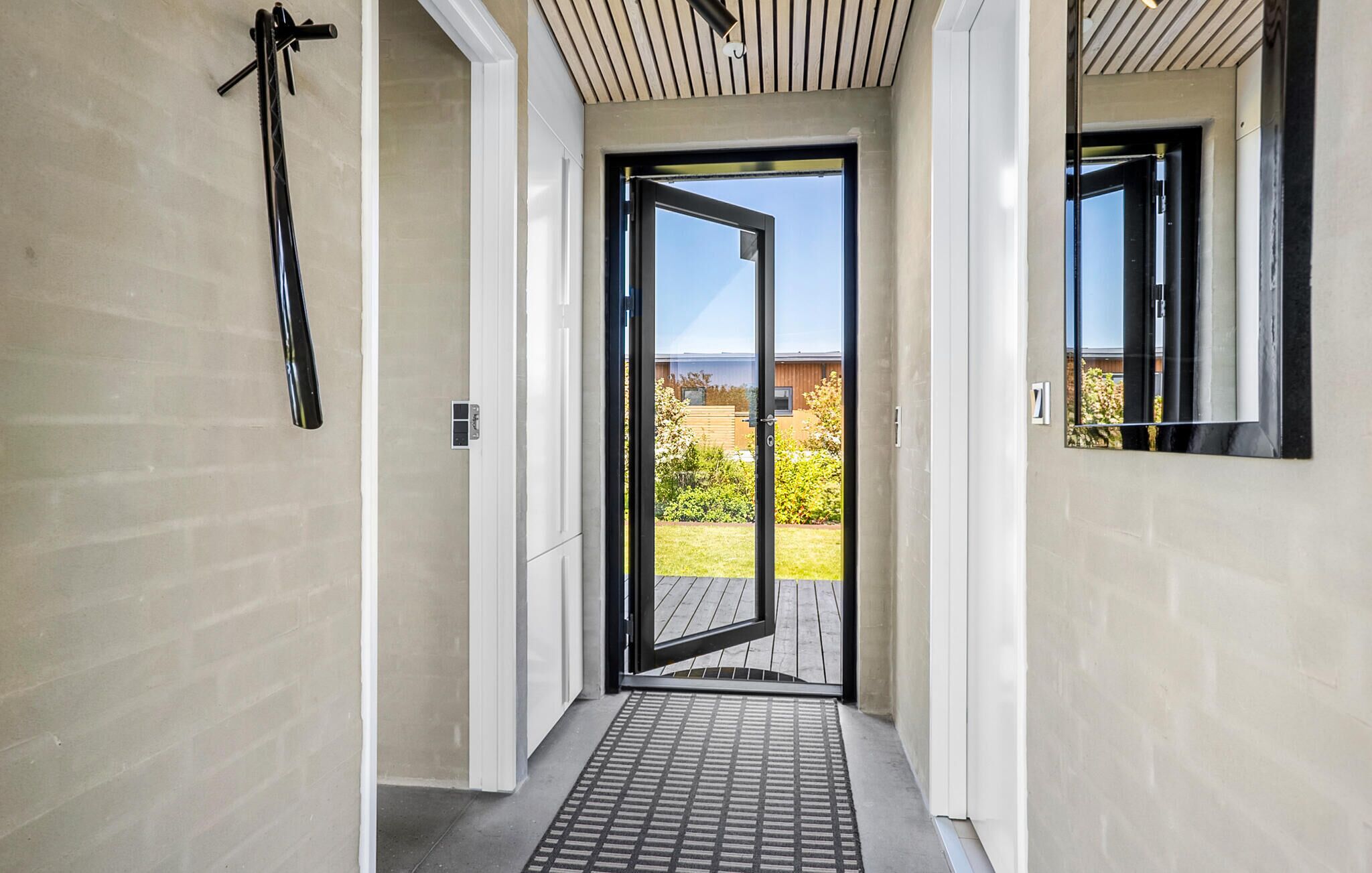 A modern hallway with a sliding glass door leading to a balcony with a view of a garden and a building.