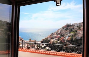 Vista costera desde un balcón con barandilla, con vistas a un pueblo de edificios coloridos y el mar.