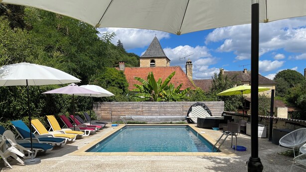 A pool area with lounge chairs and umbrellas, surrounded by greenery and a building with a tiled roof. - Gite 8p, 3*, air-conditioned heated pool, Spa, playground, wifi, ok dog cat (MONTIGNAC-LASCAUX)