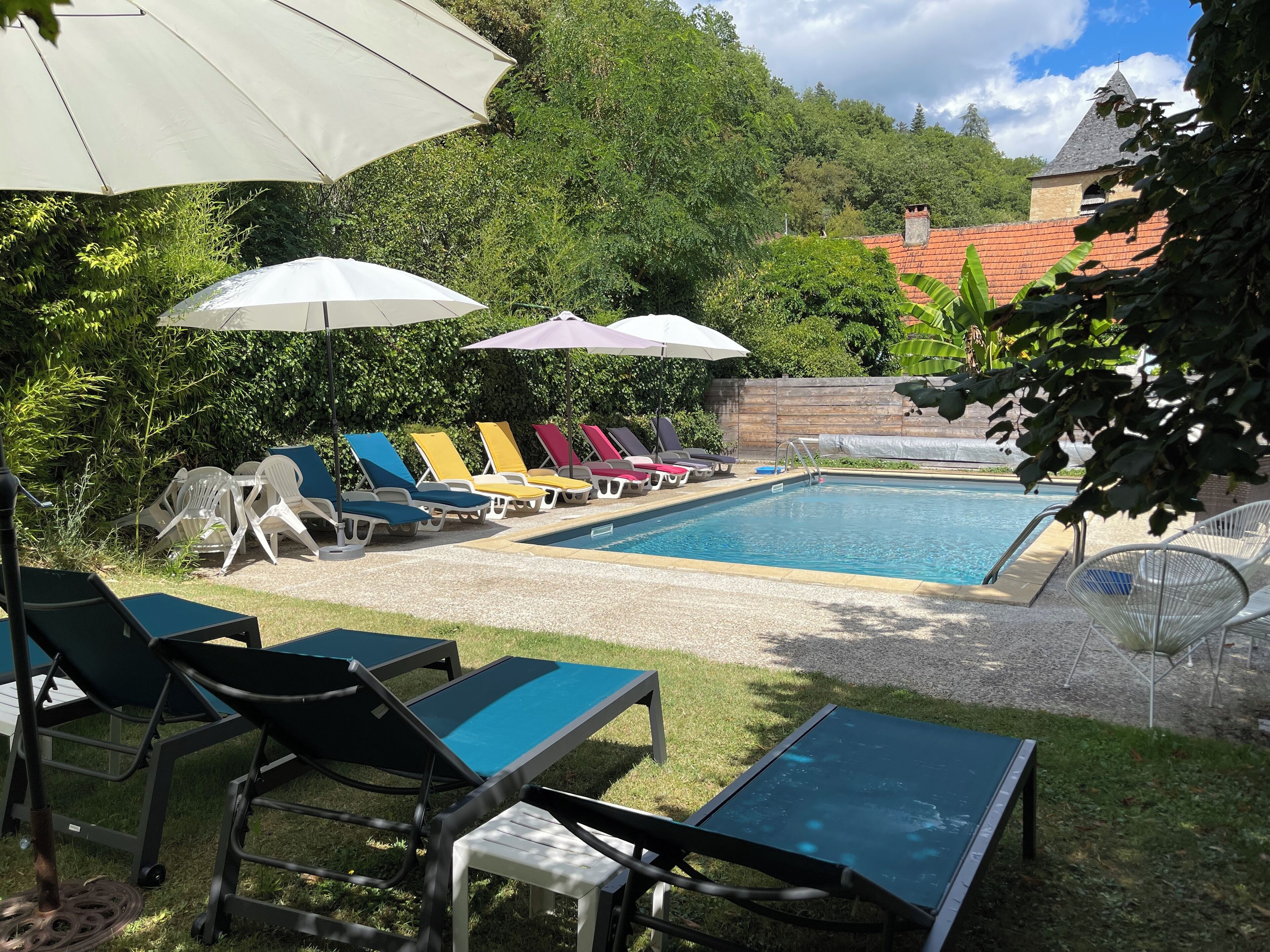 A swimming pool with lounge chairs and umbrellas, surrounded by greenery and a brick wall.
