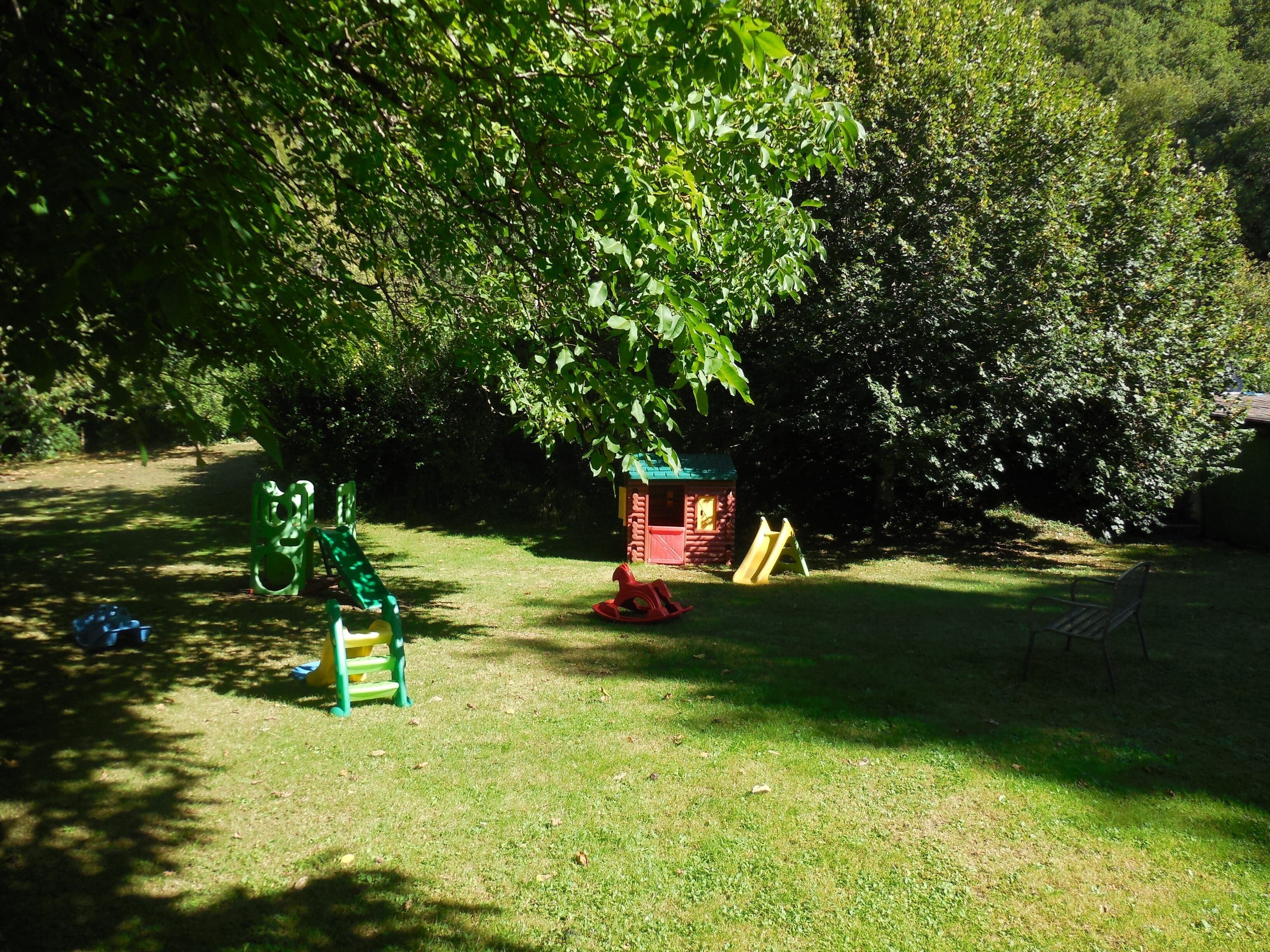A grassy outdoor area with a small red playhouse, a green slide, and a swing set.