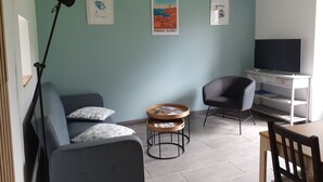 Una sala de estar con una pared color verde azulado, un sofá, un sillón, una mesa de centro, un televisor sobre un mueble bajo y fotografías enmarcadas.