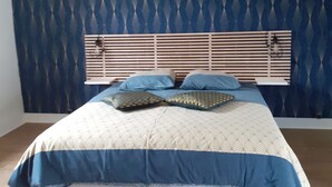 Una cama con un cabecero de estampado geométrico, una colcha azul y blanca y varias almohadas.
