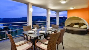 A balcony with a table set for dining, wicker chairs, and a cushioned seating area with a canopy.