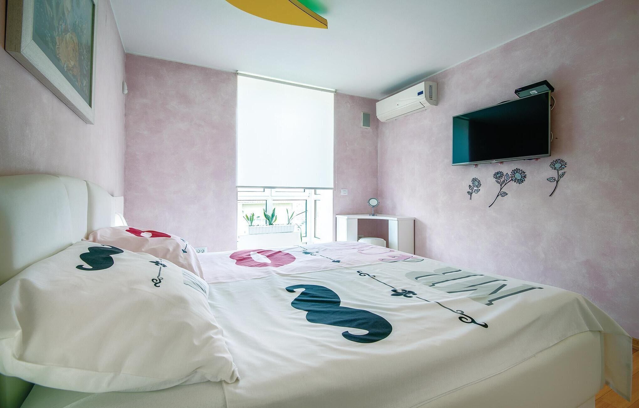 Slaapkamer met een bed, een raam, een airconditioningapparaat, een televisie en een wand met bloemmotieven.