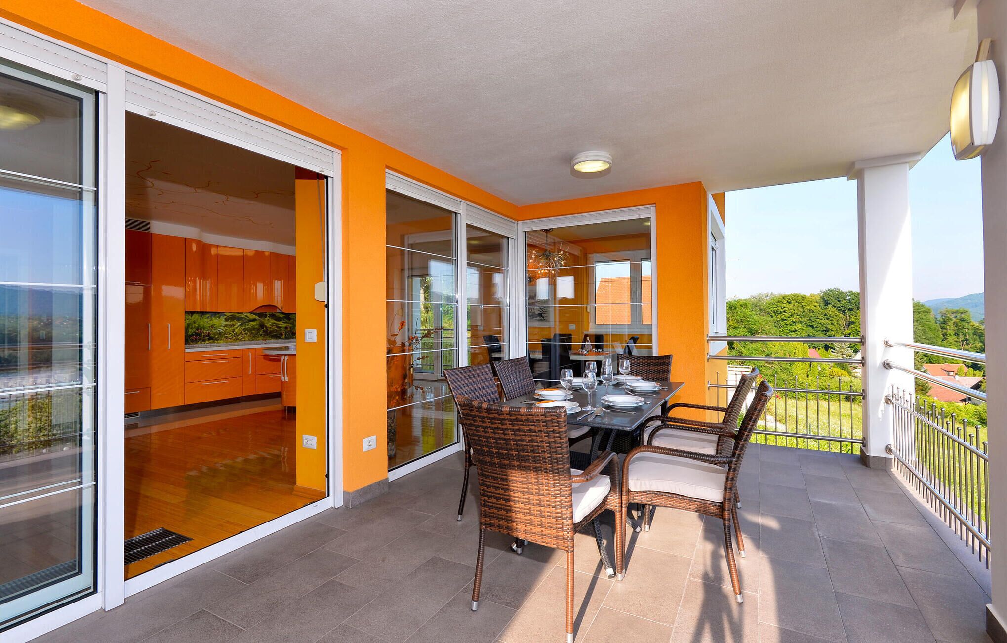 A balcony with a dining table and chairs, a view of the outdoors, and a kitchen area with orange cabinets.