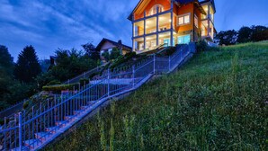A multi-story house with a staircase leading up to it, surrounded by greenery.
