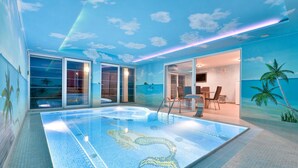 An indoor swimming pool with a tropical mural, glass doors leading to a dining area, and a ceiling with a cloud design.