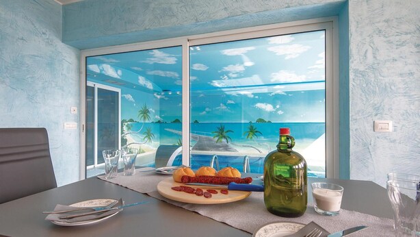 A dining table with a meal, a bottle, and a view of a beach through a window.