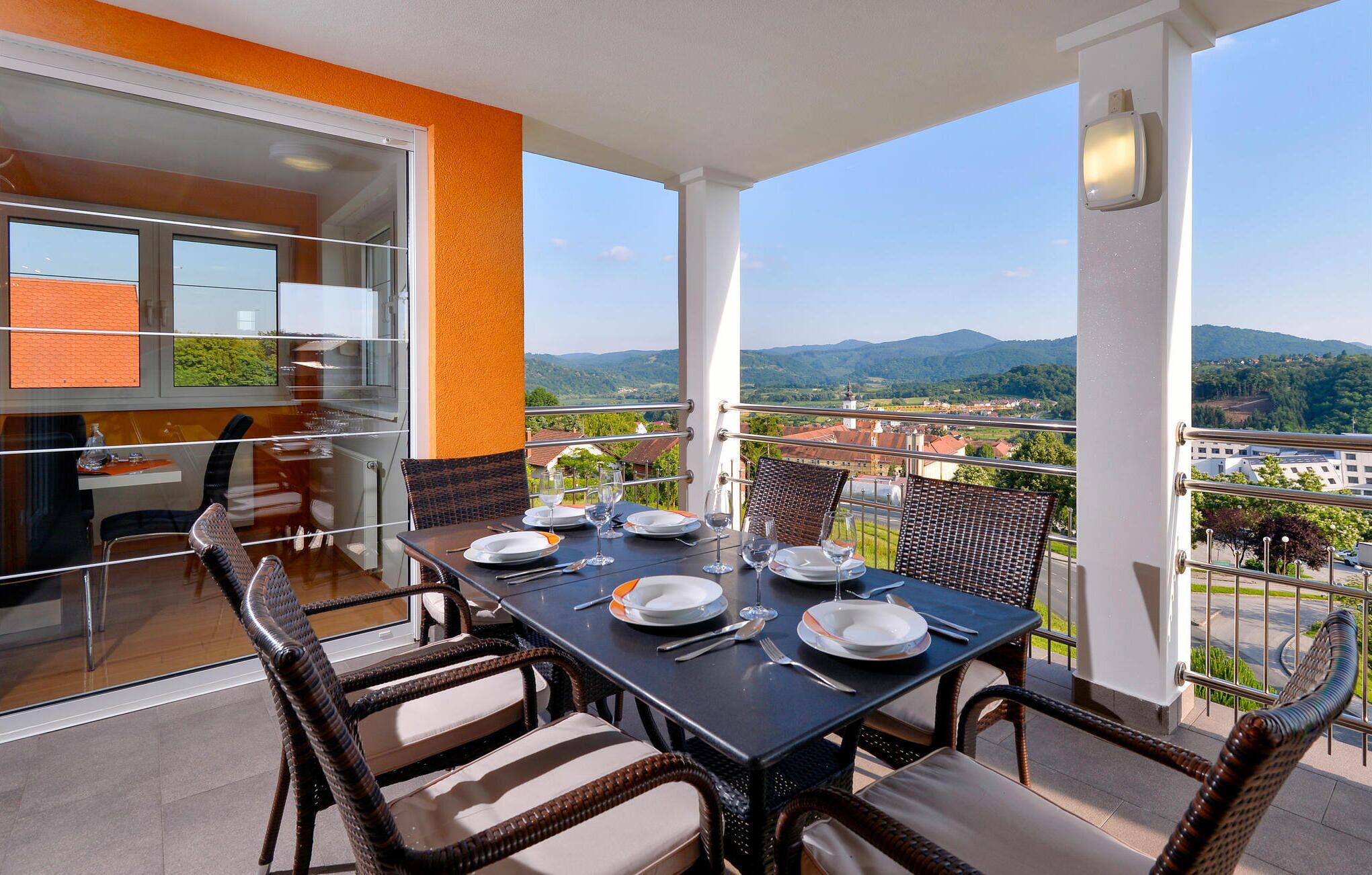 A balcony with a table set for four, overlooking a scenic view of mountains and a town.