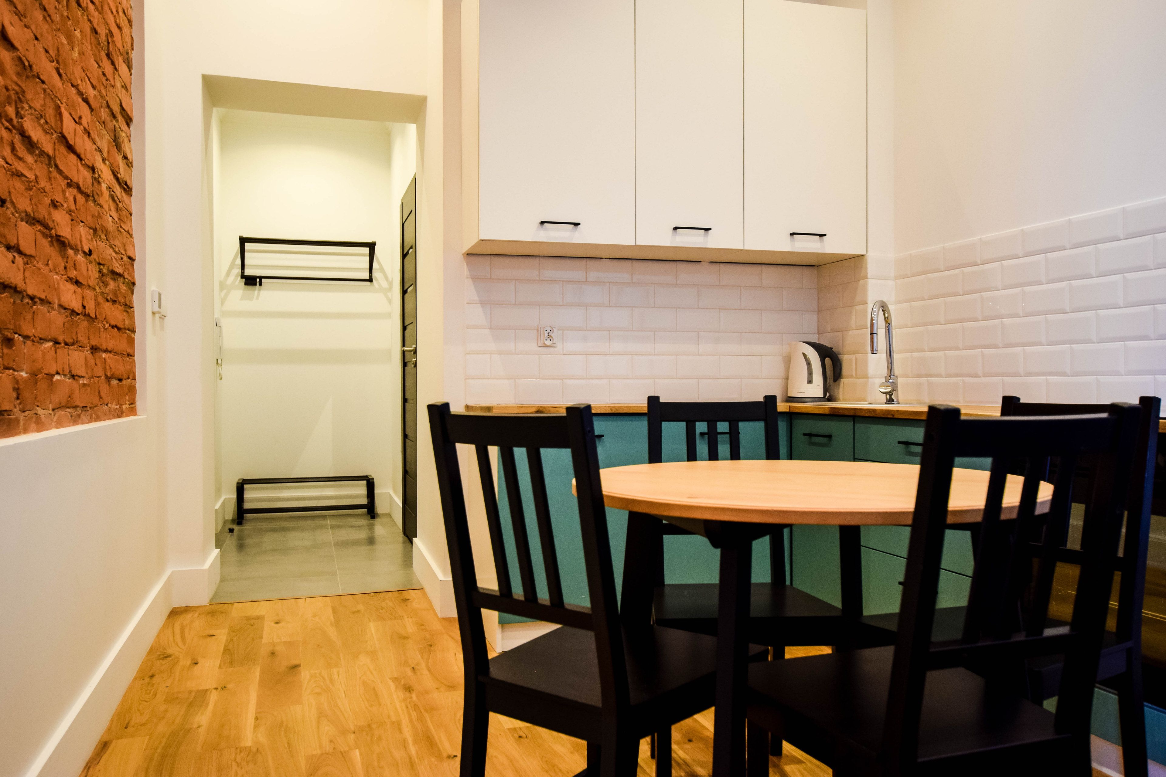 Una cocina con una mesa redonda y sillas, una pared de ladrillo y armarios blancos.
