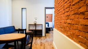 A room with a wooden floor, a round table, and a blue sofa. There is a brick wall on one side and a white wall on the other. - MB2- Gwarna 11 (Wroclaw)