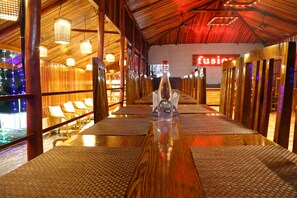 A restaurant with wooden tables and chairs, a bottle of water, and a sign that reads "fusion". - Rainforest Resort (Port Blair)