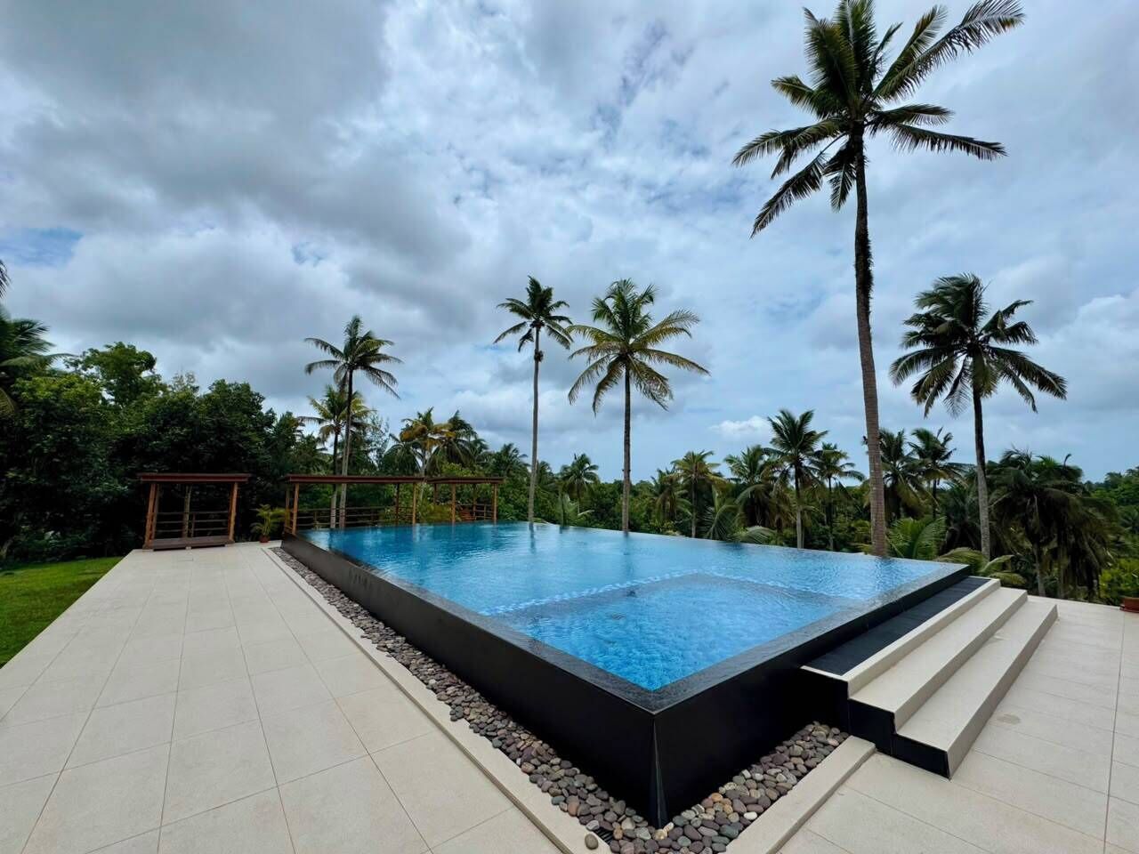 Una piscina infinita rectangular con borde negro, rodeada por una terraza con baldosas y un muro de piedra bajo.