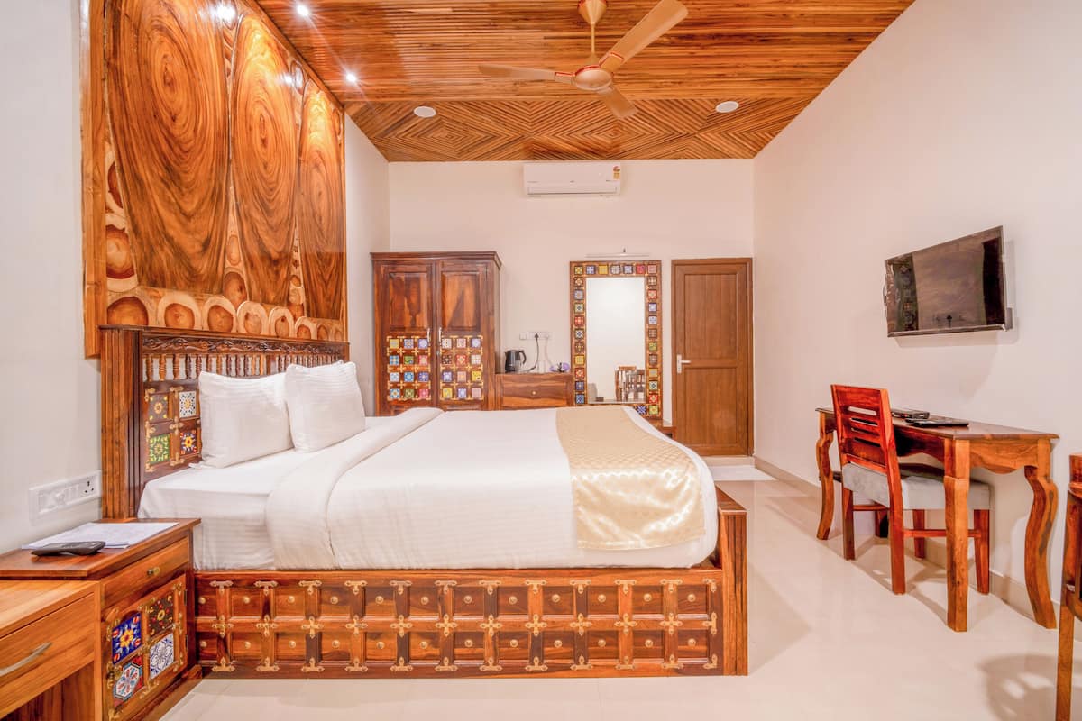 Quarto com cabeceira de madeira, uma cama, escrivaninha com cadeira, televisão e espelho.