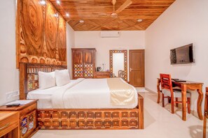 A bedroom with a wooden headboard, a bed, a desk with a chair, a television, and a mirror. - Rainforest Resort (Port Blair)