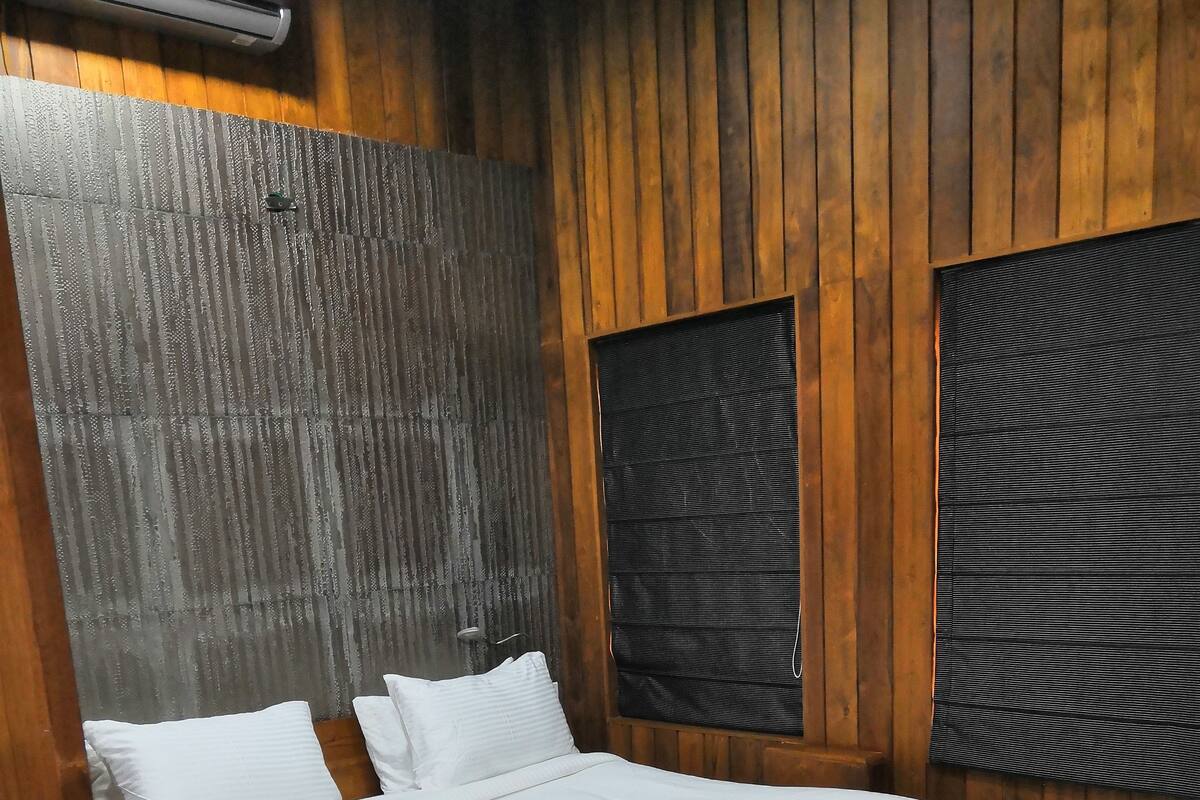 Quarto com painéis de madeira, uma cama, uma janela e ar condicionado fixado na parede.
