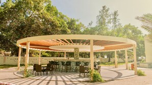 Un espace extérieur abrité, doté de tables et de chaises, entouré d’un chemin pavé de briques et de verdure.