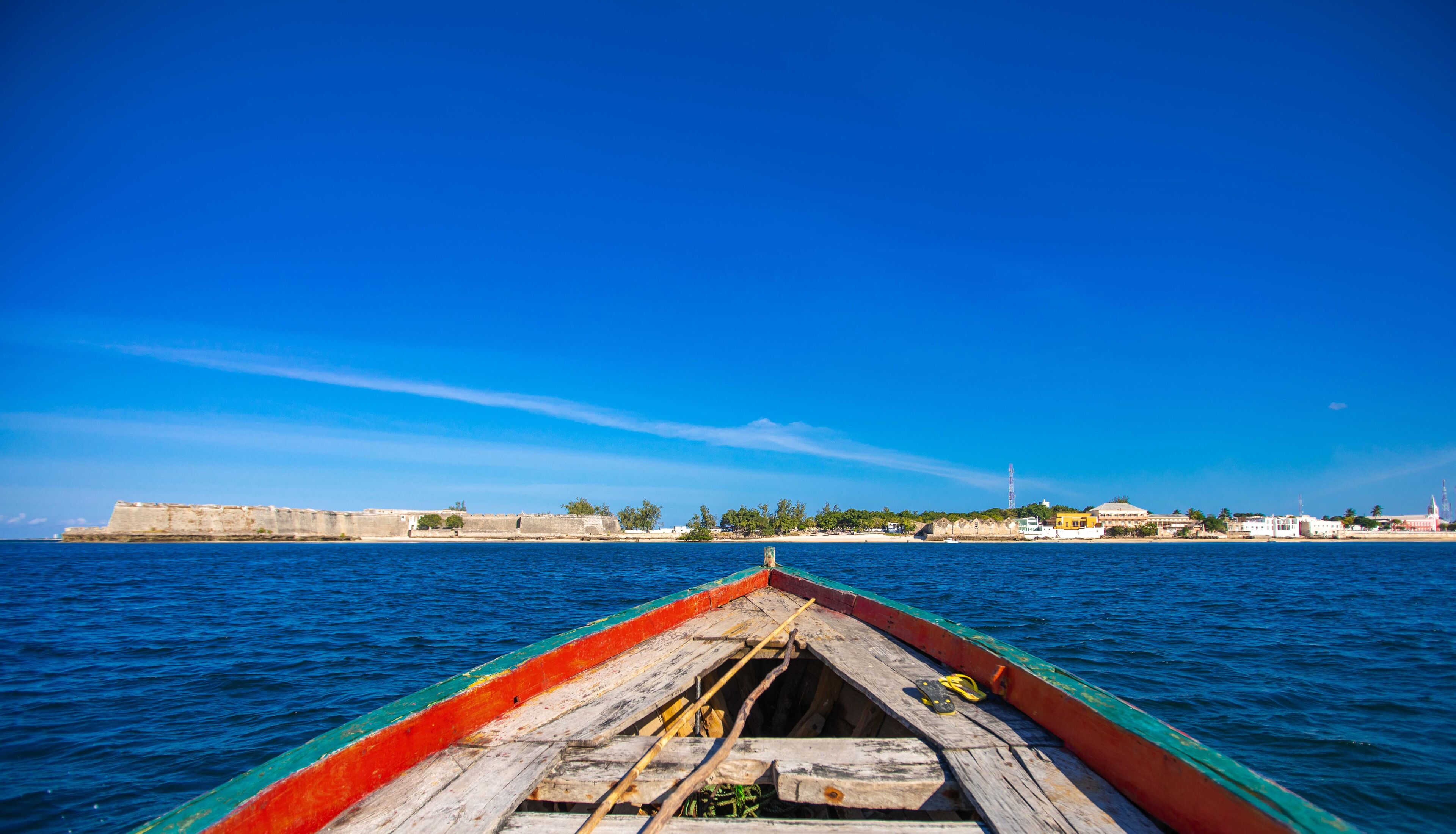 A wooden boat with a red and green hull on calm waters.