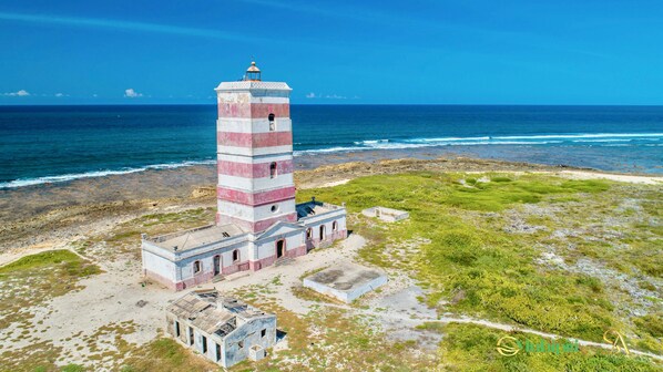 A lighthouse with a red and white striped tower, situated on a rocky coastline with the ocean in the background.