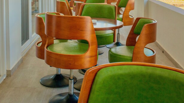 Un couloir agrémenté de chaises et de tables aux coussins verts, qui mène à un point de vue sur la plage.