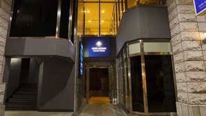 A modern hotel entrance with a glass facade, a visible staircase, and a sign indicating the hotel name.