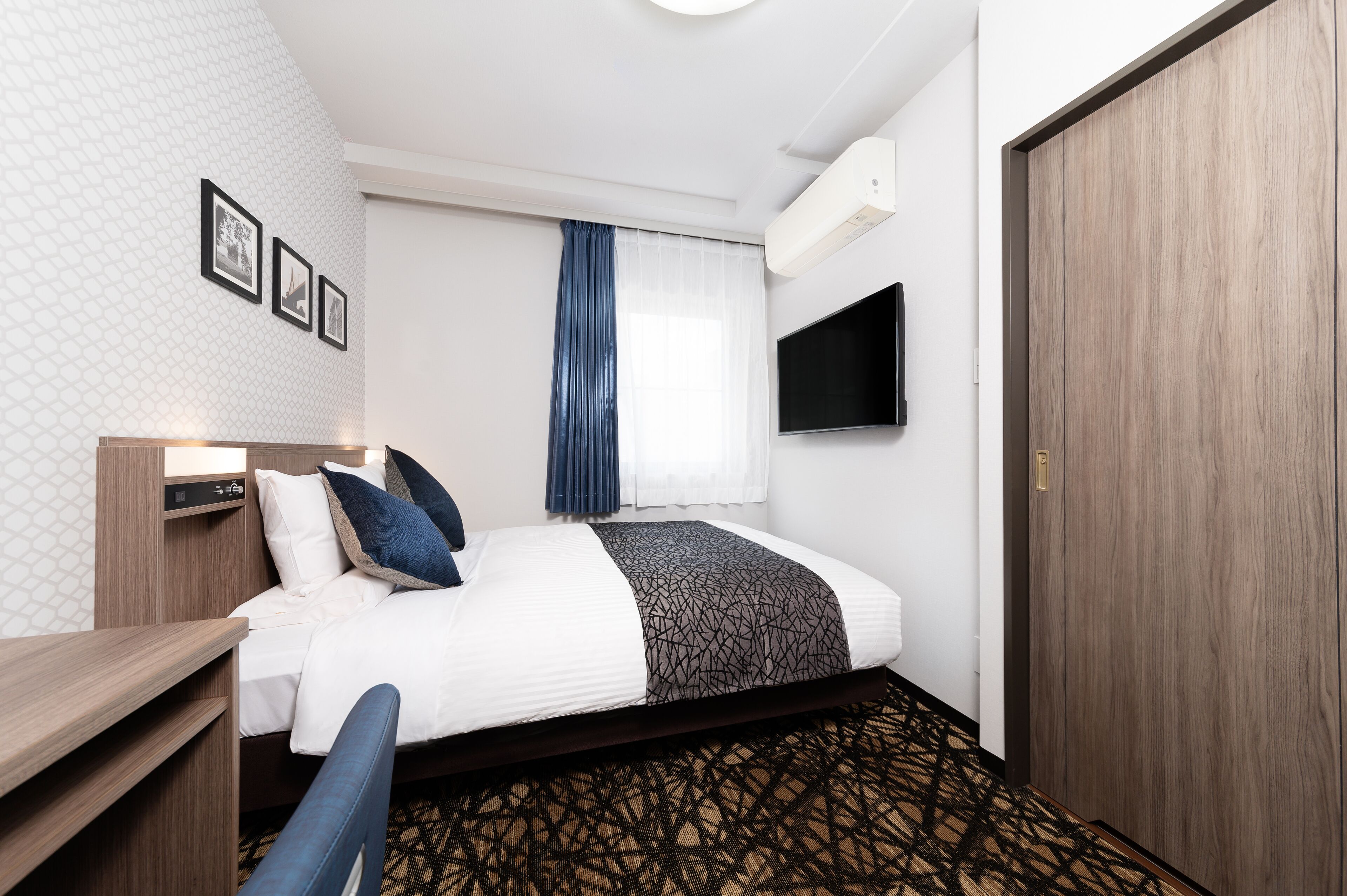 A hotel room with a bed, a desk, a TV, and a wardrobe.