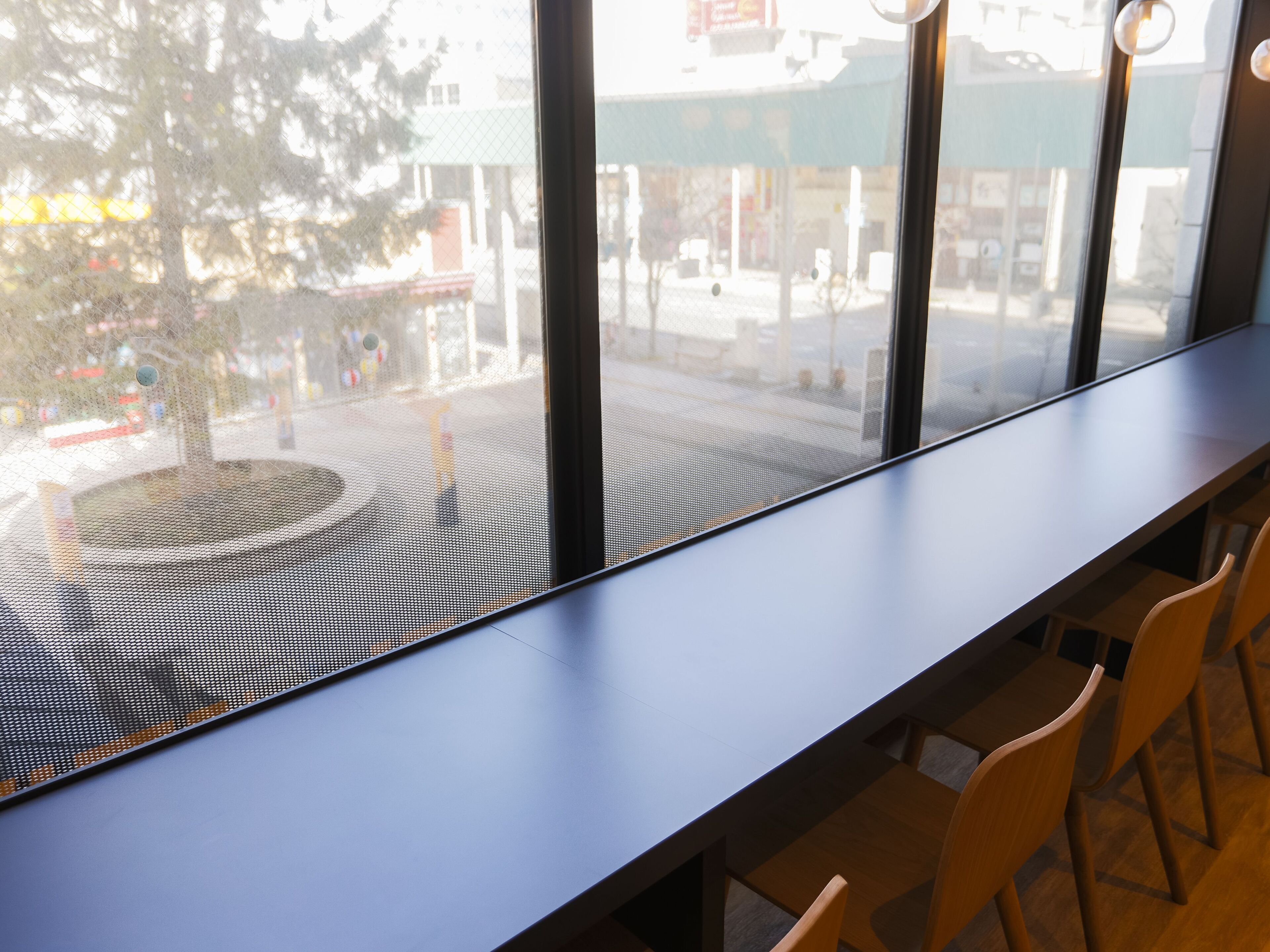 A long, dark wooden table with a metal grid barrier in front of it, and several wooden chairs are visible to the right.