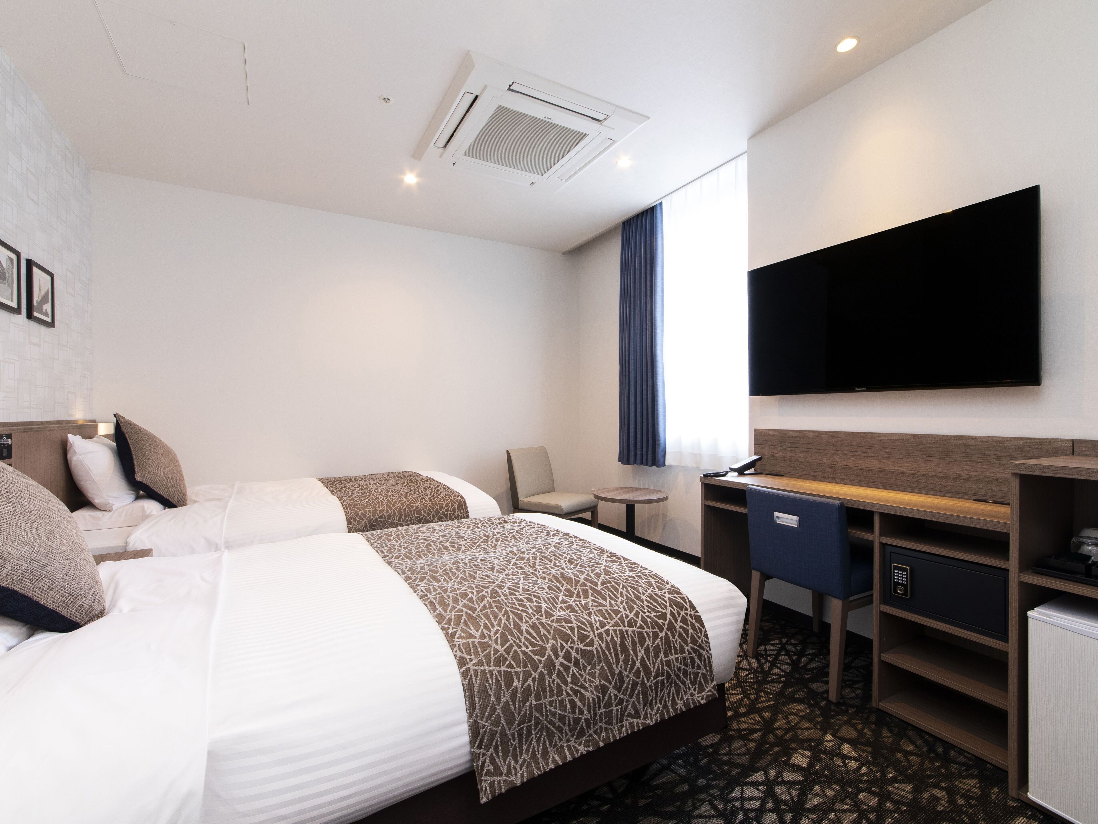 Une chambre d’hôtel avec deux lits, un bureau, une chaise, une télévision et une fenêtre avec des rideaux.